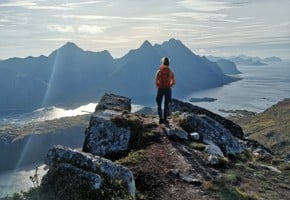 Astrid on a mountain top looking at the view and landscape beneath her. Her back is turned away from the camera.